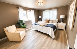 A bedroom with a bed, bedside tables, a chair, and a large window.
