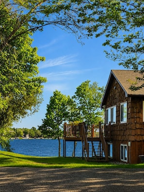 A wooden cabin with a deck overlooking a lake, surrounded by trees.