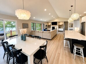 A modern kitchen with a dining area, a living room with a sofa, and a large TV.