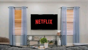 Ein Wohnzimmer mit einem flachbildfernseher an der Wand, der das Wort 'NETFLIX' anzeigt.
