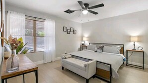 Ein Schlafzimmer mit Bett, Nachttischen, Deckenventilator und einem Fenster mit Vorhängen.