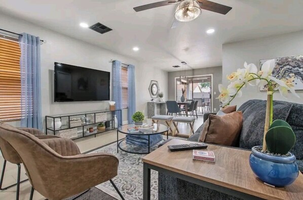 A modern living room with a flat-screen TV, comfortable seating, a coffee table, and a ceiling fan.