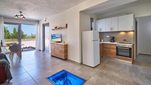 Eine moderne Küche mit weißen Schränken, einem eingebauten Backofen und einer Kaffeemaschine. Es gibt einen Essbereich mit Tisch und Stühlen sowie einen Fernseher an der Wand.