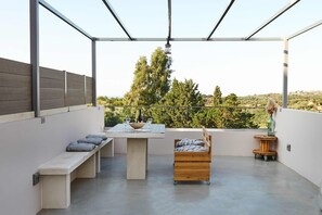 A rooftop terrace with a concrete table, benches, a wooden cabinet, and a small round table.