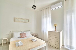 A neatly arranged bedroom with a bed, bedside table, dresser, and an air conditioning unit.