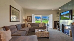 A living room with a sectional sofa, ottoman, fireplace, TV, and a view of a golf course. - Beautiful Desert Falls home right on the golf course (Palm Desert)