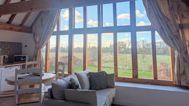 Una habitación acogedora con un ventanal grande, vigas de madera, un sofá, una mesa de comedor y una zona de cocina.