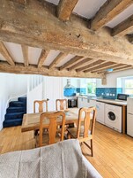 A rustic kitchen with exposed wooden beams, a dining area with wooden chairs, and a blue-tiled backsplash.