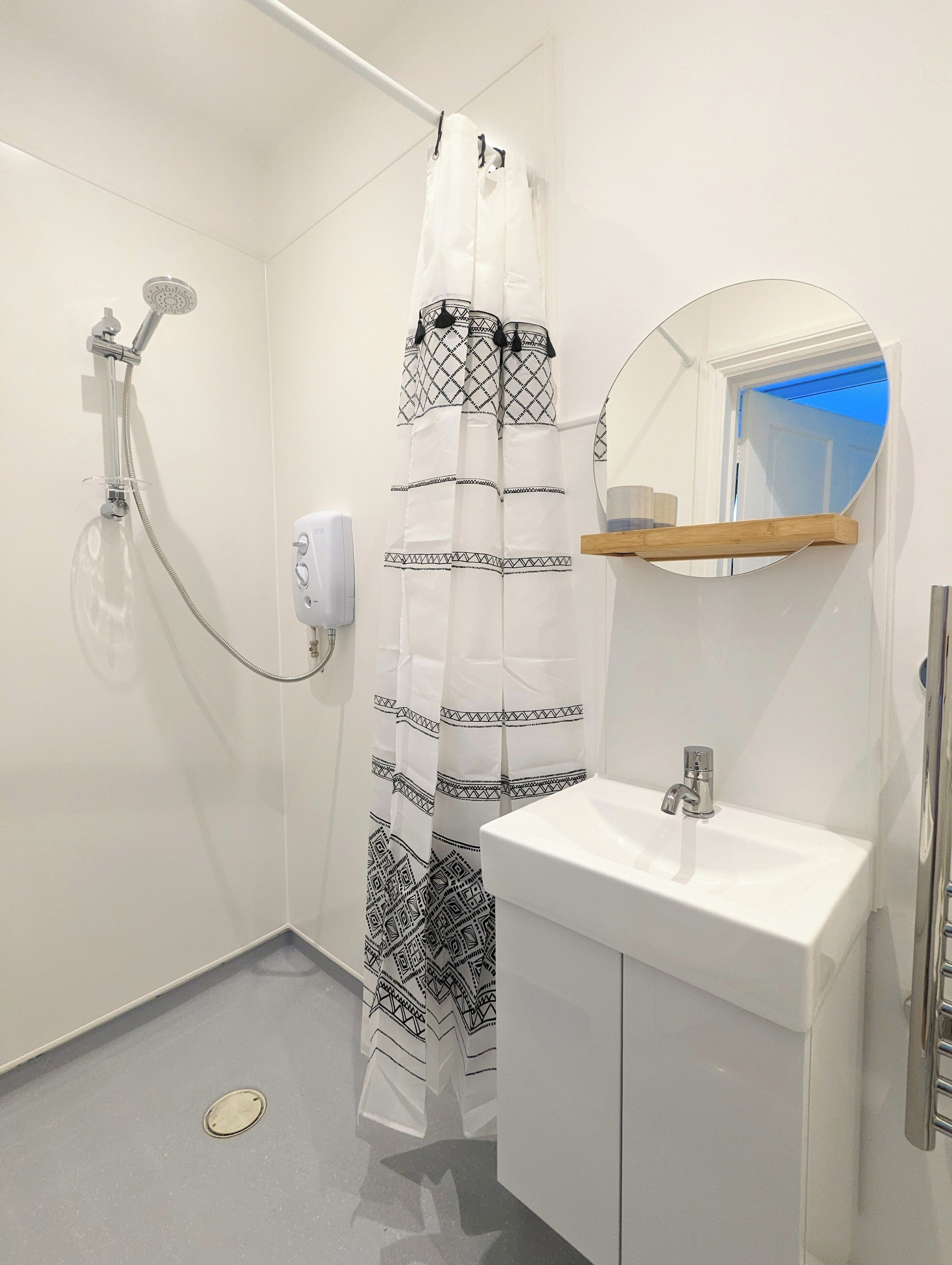 A bathroom with a shower, a sink, a mirror, and a towel rack.