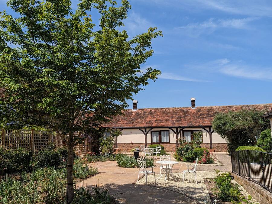 A courtyard with stone flooring, outdoor seating, and a building with a tiled roof.