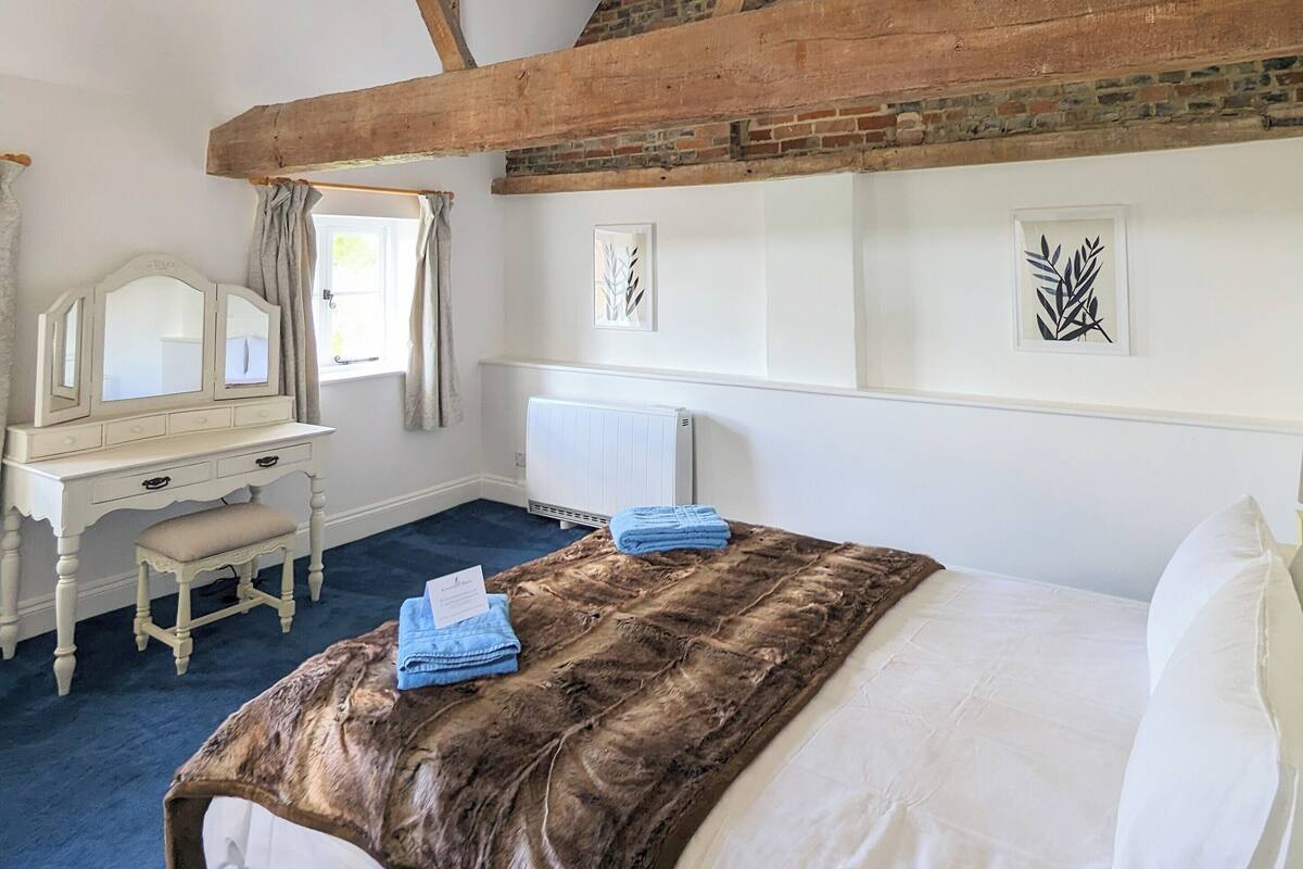 A bedroom with a large bed, a wooden desk, and a mirror.