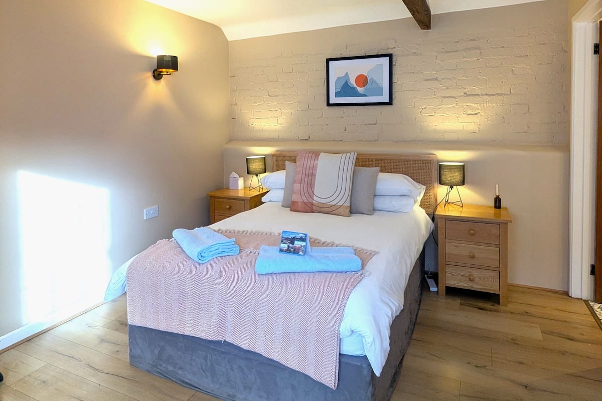 A bedroom with a large bed, wooden beams, a brick wall, and a framed picture.