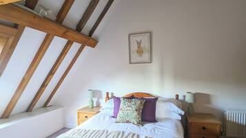 A bedroom with a sloped ceiling, a bed with white bedding and multiple pillows, two bedside tables with lamps, and a framed picture on the wall.