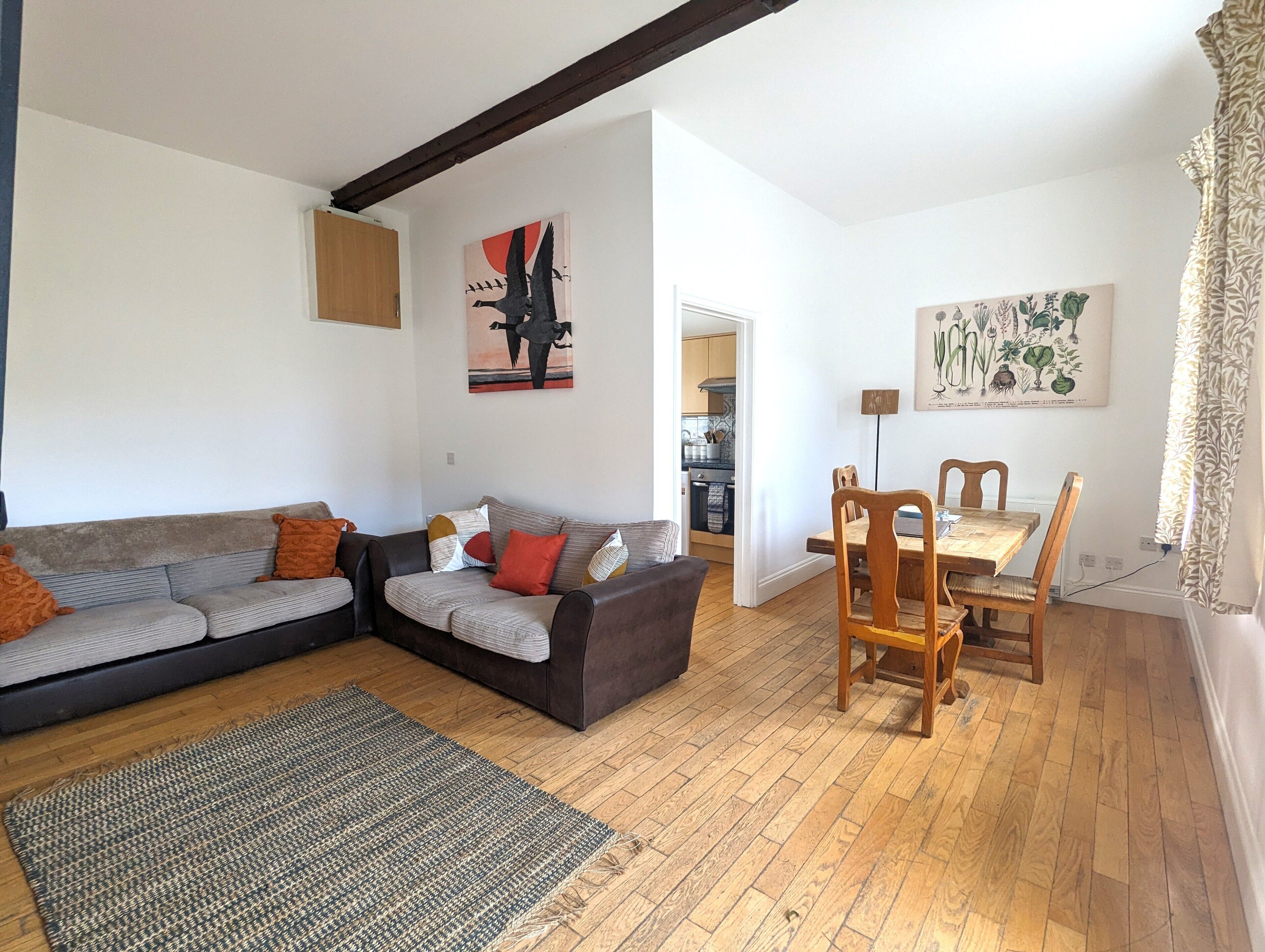 A living room with a sofa, a rug, a dining table with chairs, and artwork on the walls.