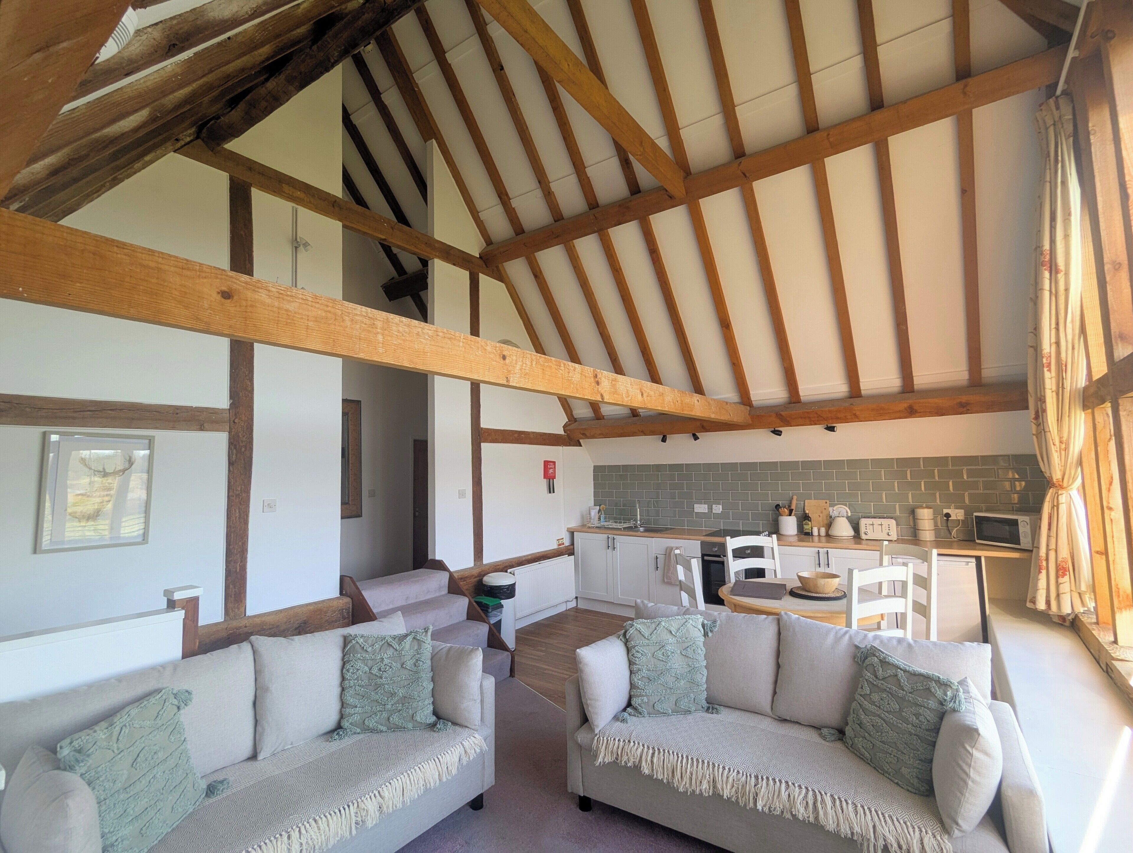 A spacious living area with two sofas, a kitchen in the background, and a high wooden ceiling.