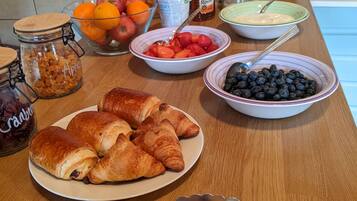 Una mesa de desayuno con pasteles, frutas y frascos de conservas.