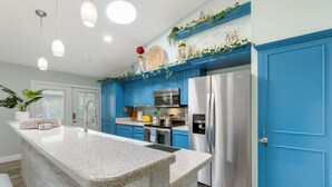 A kitchen with blue cabinets, a stainless steel refrigerator, and a marble island.