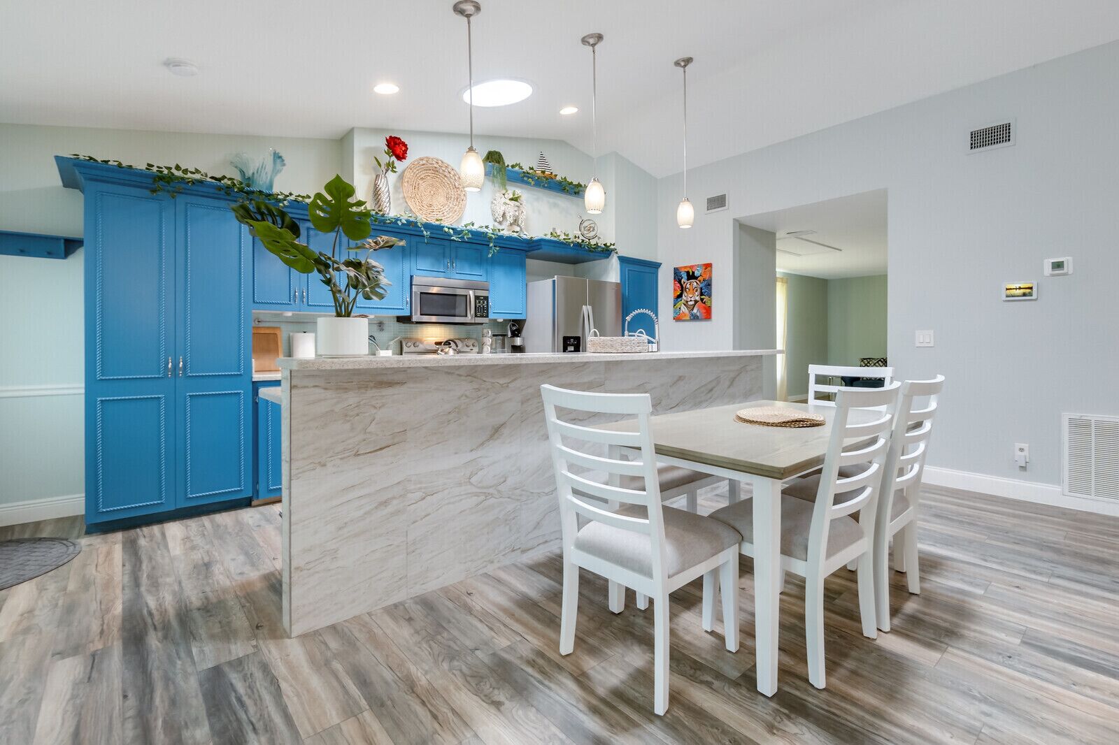 Una cocina moderna con armarios azules, una isla de mármol, sillas blancas e iluminación colgante.