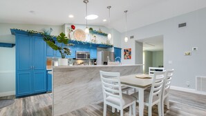 A modern kitchen with blue cabinets, a marble island, white chairs, and pendant lighting.