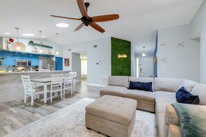 Un salon moderne avec un canapé beige, un coin repas avec des chaises blanches et une cuisine avec des meubles bleus.