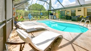 A covered outdoor swimming pool with lounge chairs and a barbecue area.