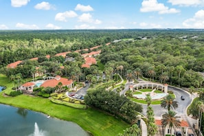 An aerial view of a residential area with houses, a swimming pool, and a landscaped park with a fountain.
