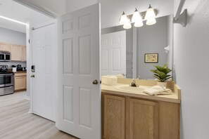 Bathroom features a large mirror, sink, and countertop, with a wooden vanity and wall-mounted lights.