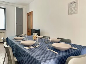 A dining area with a table set for four, including plates, bowls, cutlery, and glasses. - APPARTAMENTO A 900 METRI DAL LAGO MAGGIORE (Arona)