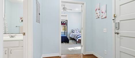 Un pasillo con suelo de madera que conduce a un dormitorio con cama y mesita de noche.