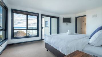 Ein modernes Hotelzimmer mit einem großen Bett, einem Holznachttisch, einem an der Wand befestigten Fernseher und einem Balkon mit Meerblick.