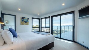 A modern bedroom with a large bed, a painting, and a view of the sea.