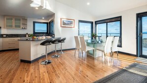 A modern kitchen with a central island, bar stools, and a dining area with a glass table and chairs.
