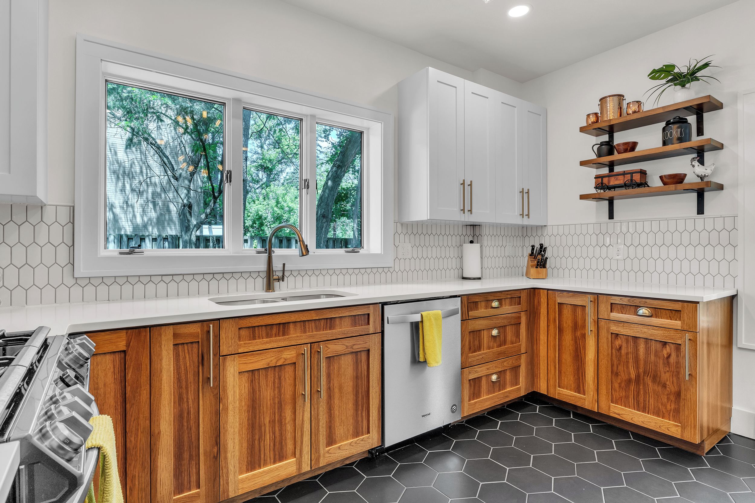 A modern kitchen with wooden cabinets, a white countertop, a built-in dishwasher, and a window with a view of trees.