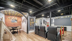 A room with a brick wall, a wooden floor, a table with chairs, a projector screen, and a tent.
