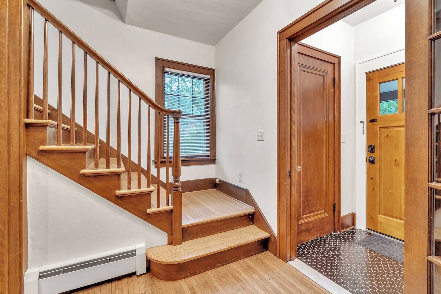 A wooden staircase with a handrail, a window with blinds, and a door with a glass panel.