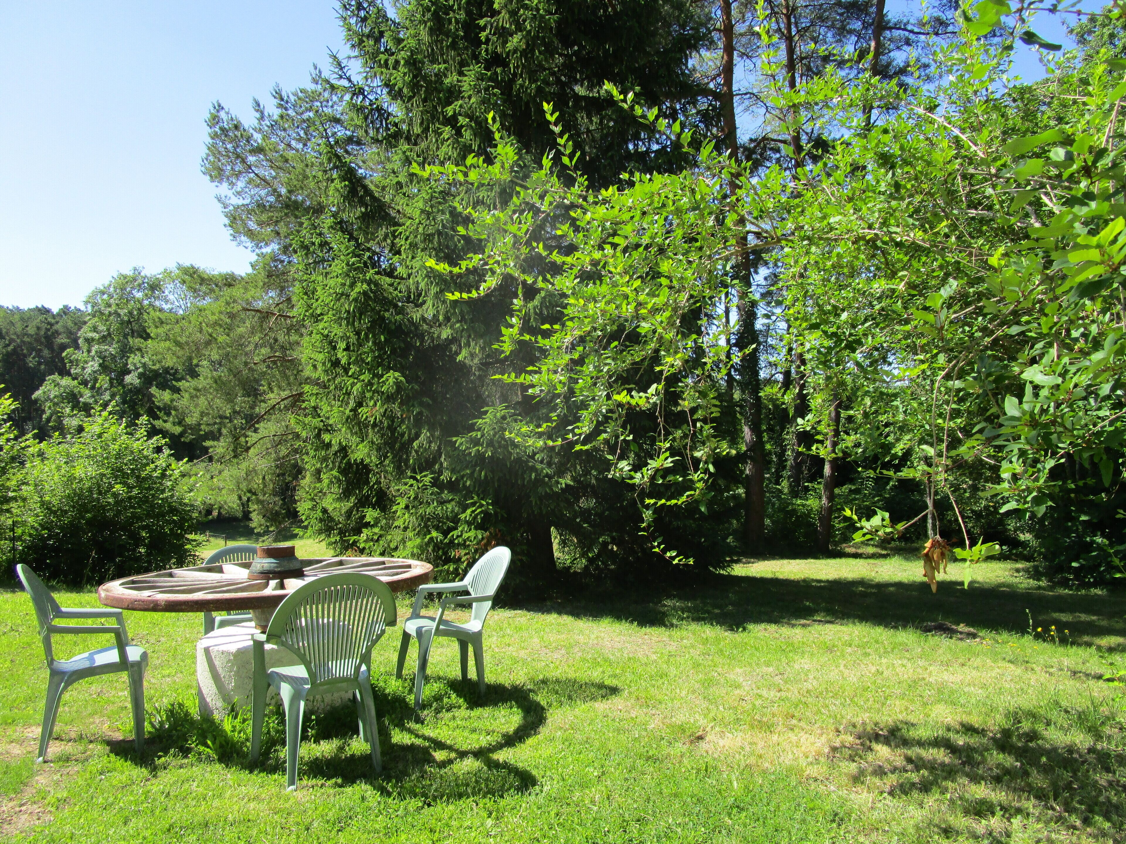 A circular outdoor table with chairs, surrounded by a grassy area and trees.
