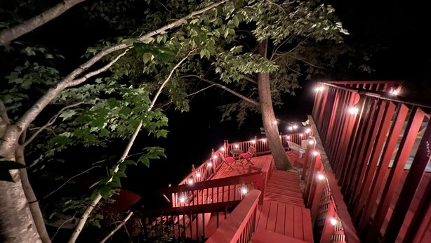A wooden staircase with railings, surrounded by trees and illuminated by string lights.