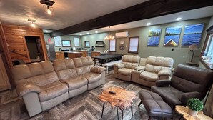 A spacious living area with leather sofas, a herringbone wood floor, and a kitchen in the background.