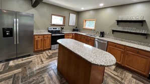 A modern kitchen with granite countertops, stainless steel appliances, wooden cabinets, and a herringbone-patterned floor.