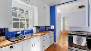 Cozinha moderna com armários brancos, máquina de lavar louça Bosch, forno de aço inoxidável e uma parede azul de destaque.