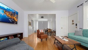 Uma sala de estar moderna com sofá, mesa de centro, TV na parede e uma pintura com vista para a cidade.