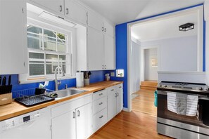 A modern kitchen with white cabinets, a Bosch dishwasher, a stainless steel oven, and a blue accent wall.