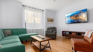 Uma sala de estar moderna com um sofá verde, uma poltrona de couro marrom, uma mesa de centro de madeira e uma TV de tela plana na parede.