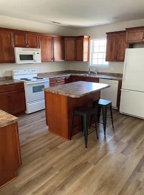Una cocina con armarios de madera, encimera de granito, refrigerador blanco, estufa y pileta.