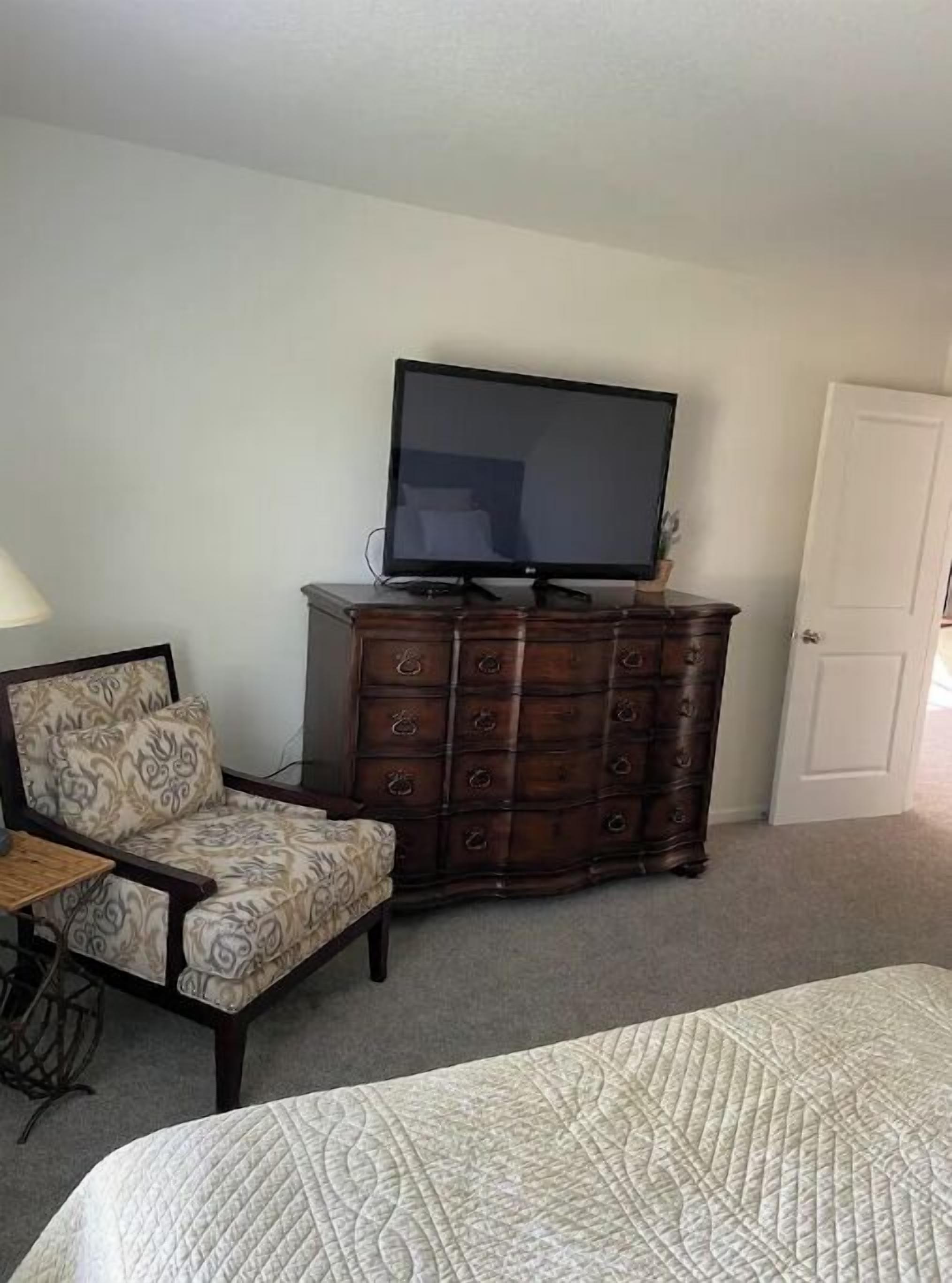 Een slaapkamer met een bed, een dressoir met een televisie erop, een stoel en een lamp.