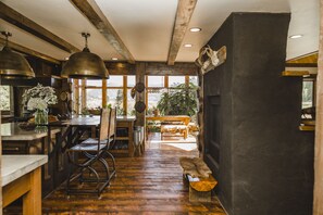A rustic kitchen with wooden floors, a dining area with a bench, and large windows overlooking a forested area. - Luxury ranch cabin for 12, dog friendly with hot tub, private valley with creek! (Creede)