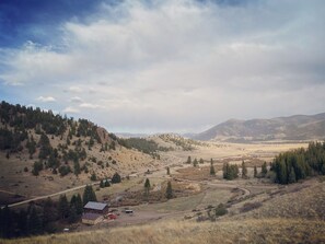 A rural landscape with a house, a dirt road, and surrounding hills. - Luxury ranch cabin for 12, dog friendly with hot tub, private valley with creek! (Creede)