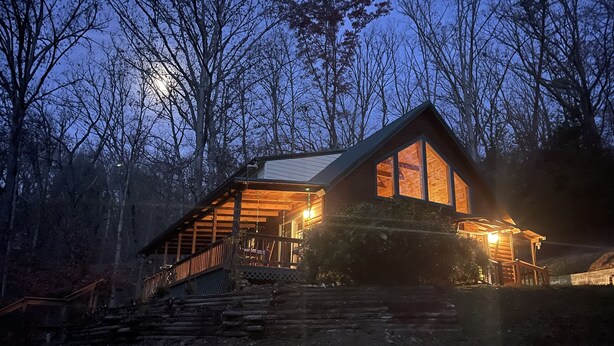 A cabin with a wooden exterior, large windows, and a porch with steps leading up to it.