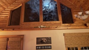 A cabin interior with a large triangular window, wooden ceiling, and a bear warning sign.