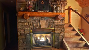 A stone fireplace with a glass front, a wooden shelf above it, and a sign that reads "Mountains are calling".